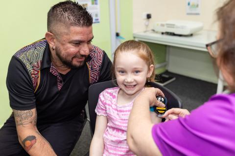 Kyla receives an immunisation using the PCHF's innovative Buzzy Bee device, supported by her dad Kyle.
