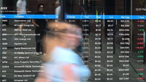 People walk past a screen showing stock information at the ASX